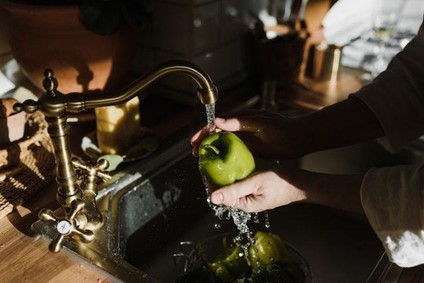 Running water from a tap and a set of hands washing a green apple.
