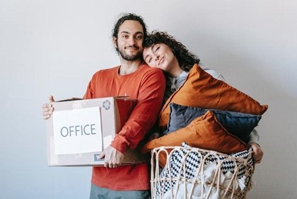 A couple hugging with a basket of pillows and a labelled box while making their long-distance move easier.