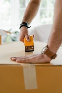 A person taping up a moving box so as not to make any moving day mistake to look out for.